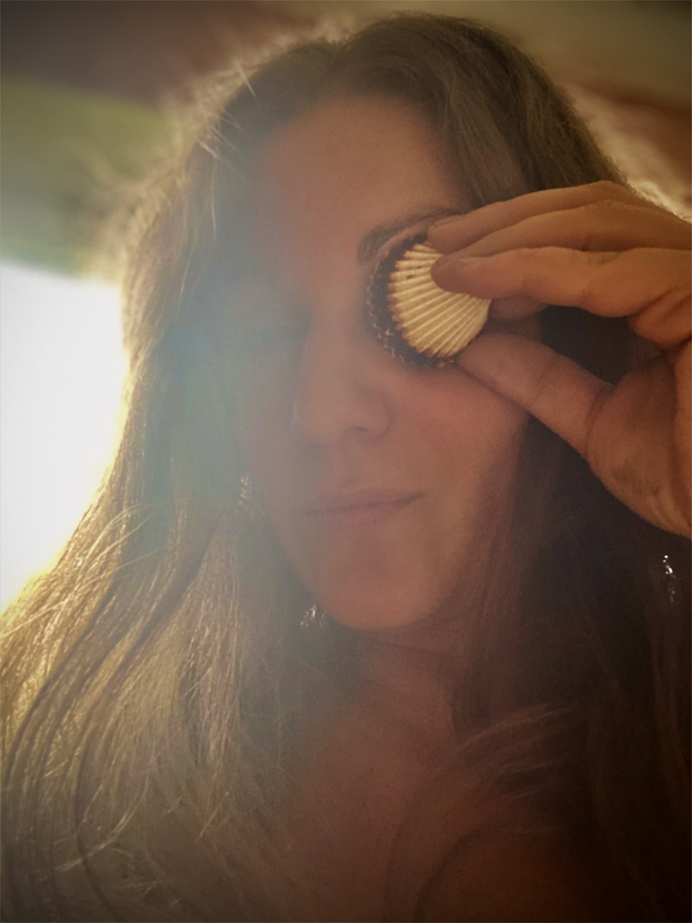 A woman holding a seashell over her left eye